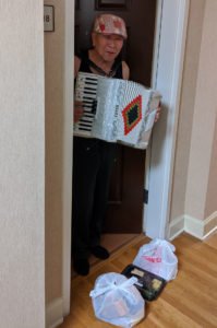 A older man greets CPACS staff bringing him meals with accordion music.