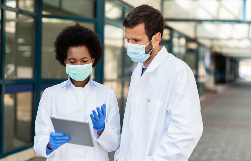 Two healthcare workers wearing masks and gloves looking at tablet