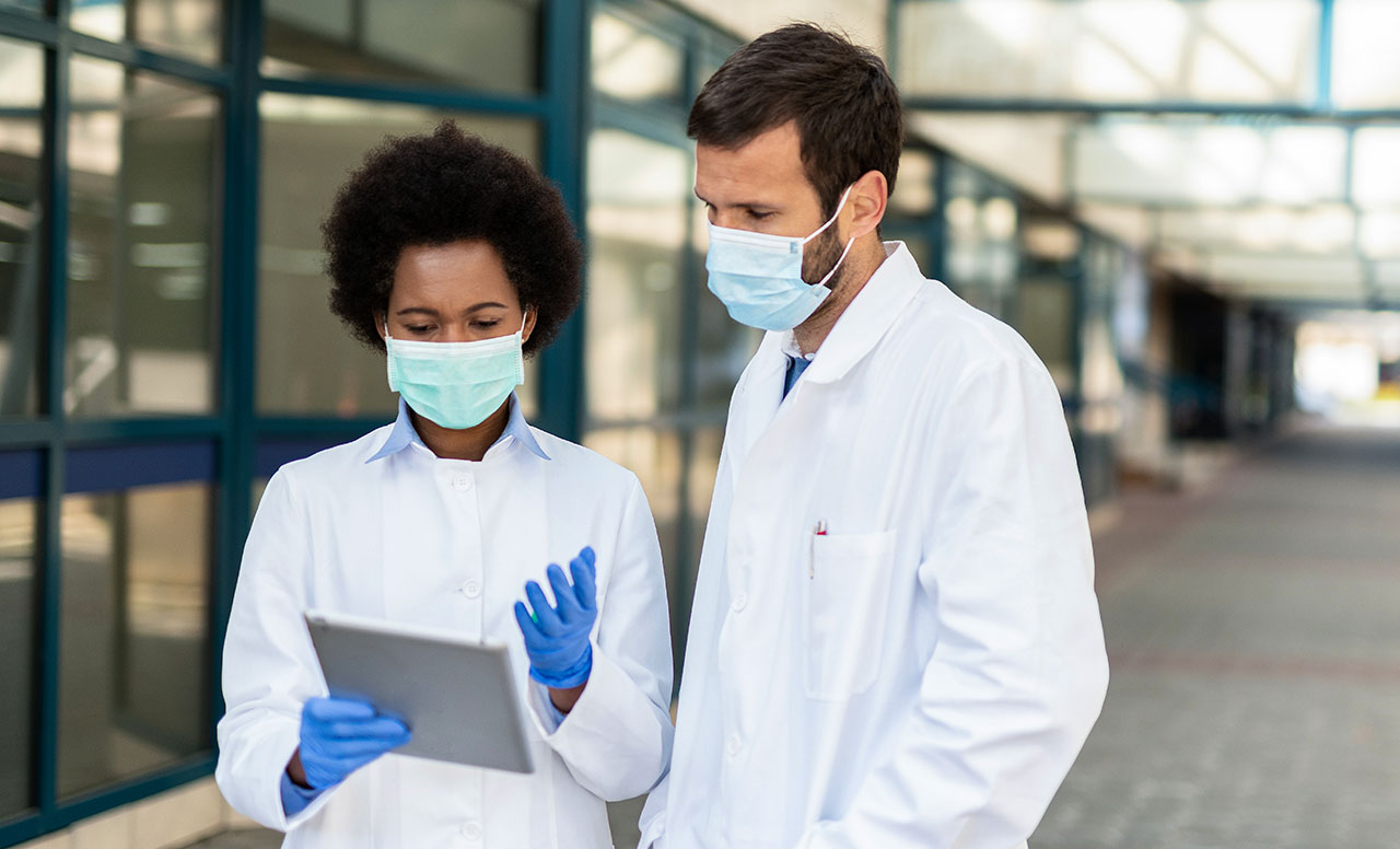 Two healthcare workers wearing masks and gloves looking at tablet