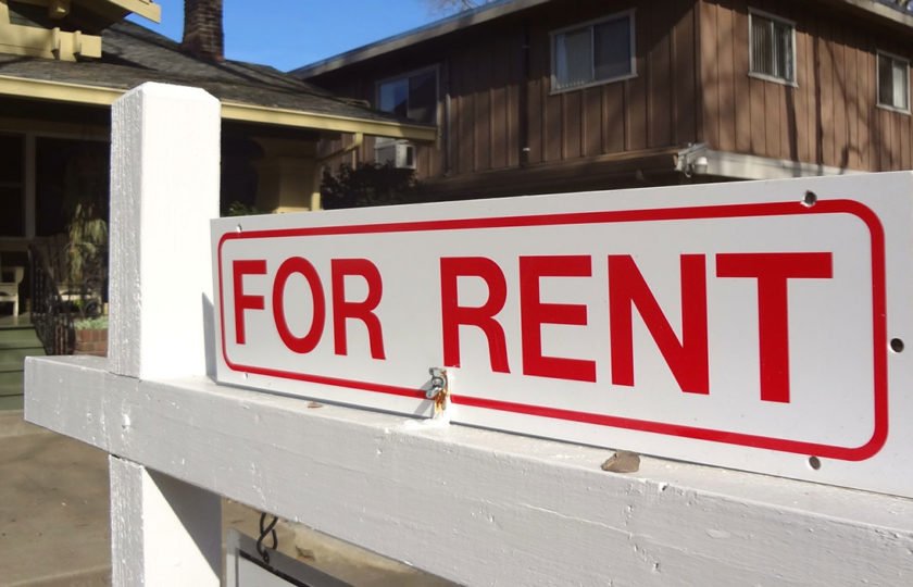 A “For Rent” sign hangs in front of a house.