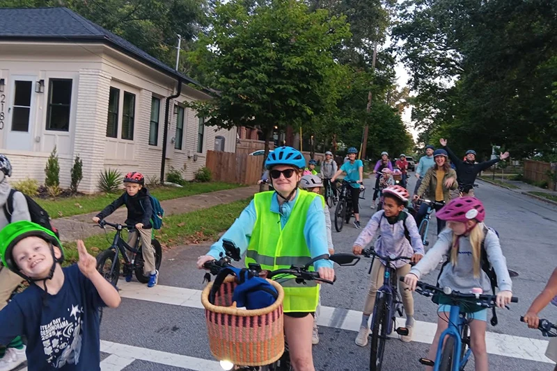 Group of school students with backpacks riding bikes to school alongside parents.