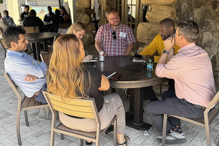 Group of about 6 people sitting outside around the table having a discussion