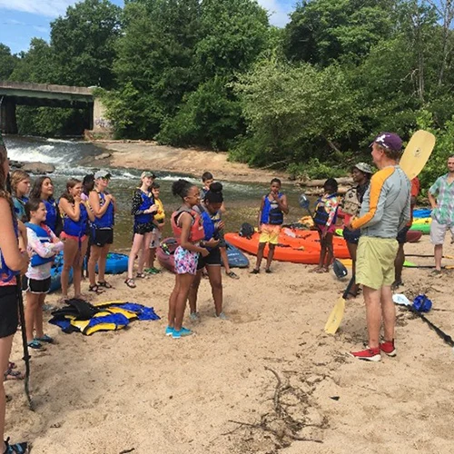 An instructor speaking to a group of people at the edge of the river.